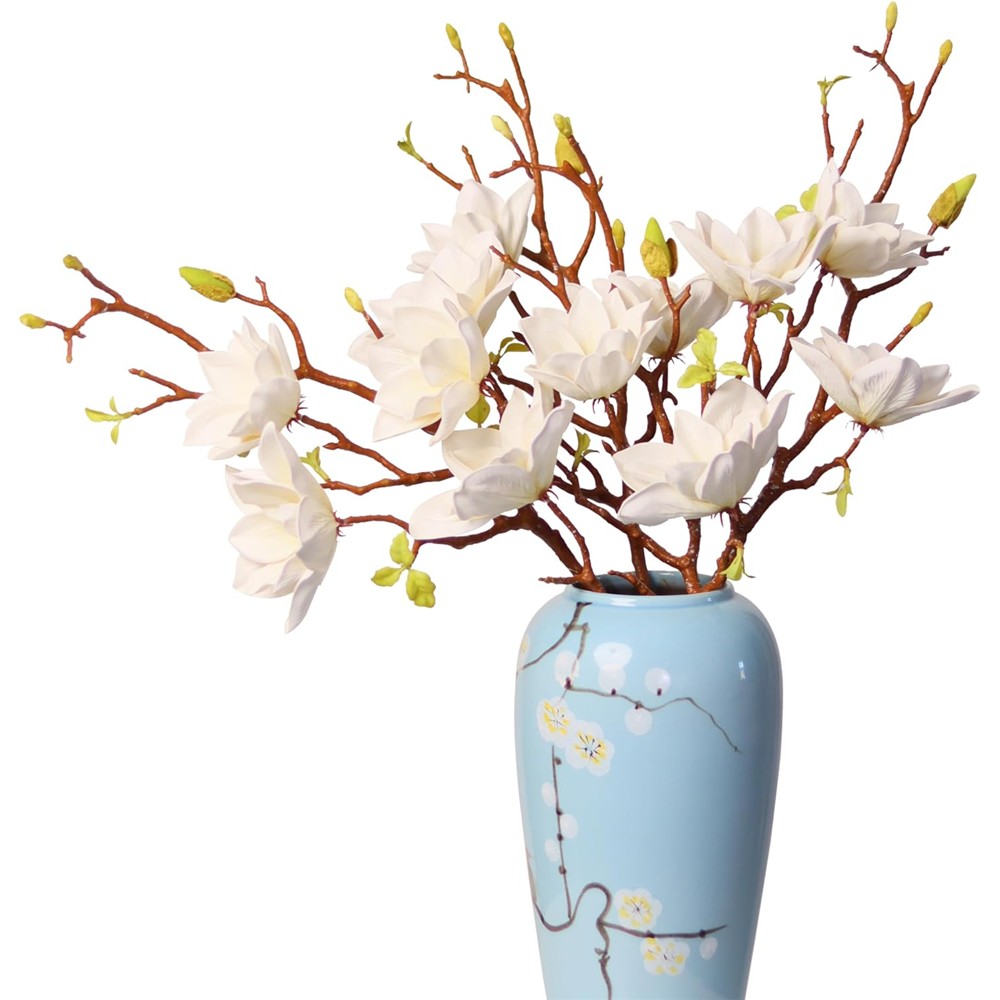 White artificial magnolia branches with open flowers and buds in a styling vase